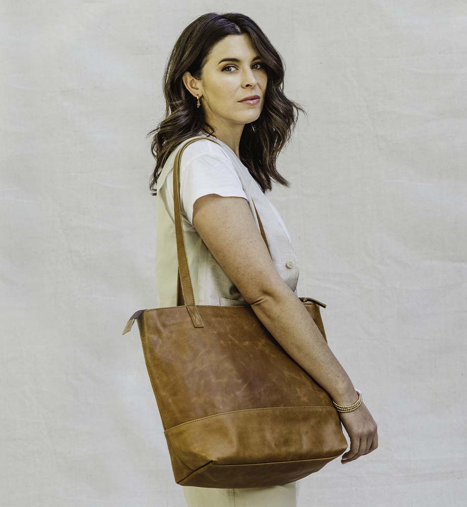 Woman standing sideways to the camera with a tan leather tote