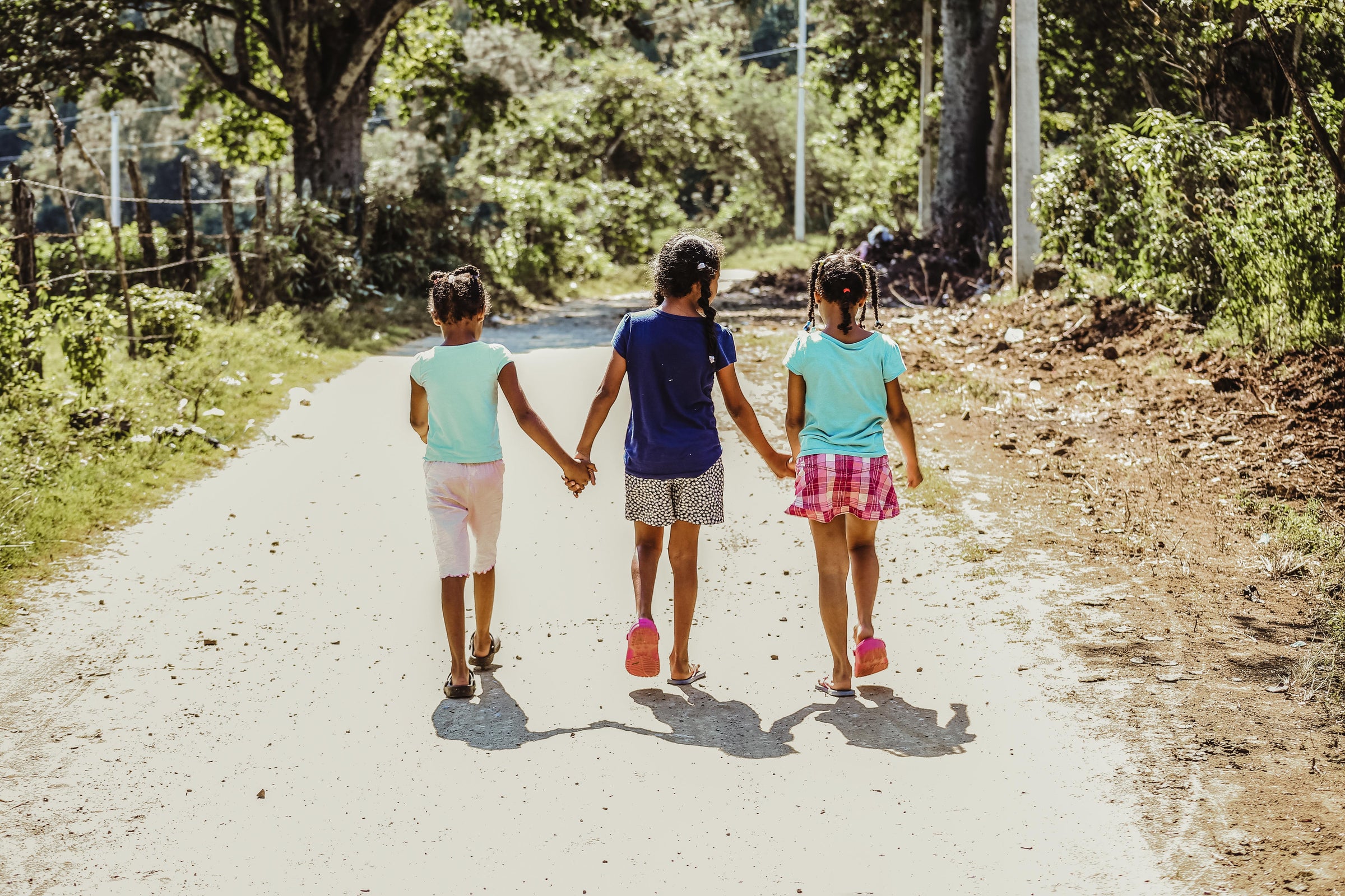 Three Children walk down a path holding hands with trees around them