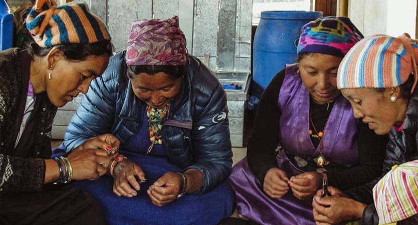 4 women gather around to make jewelry