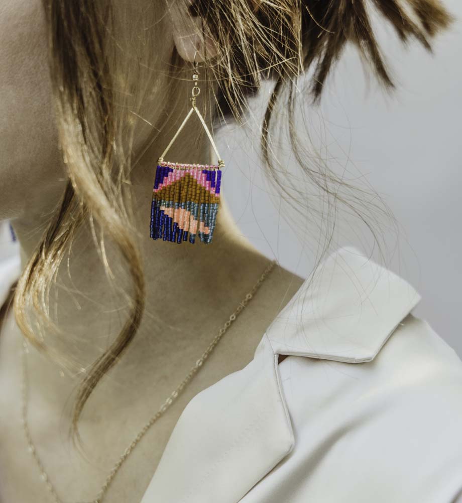Women with white top on wearing multicolored fringe earrings and gold necklace