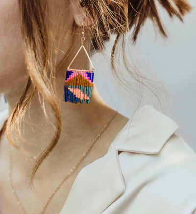 Women with white top on wearing multicolored fringe earrings and gold necklace
