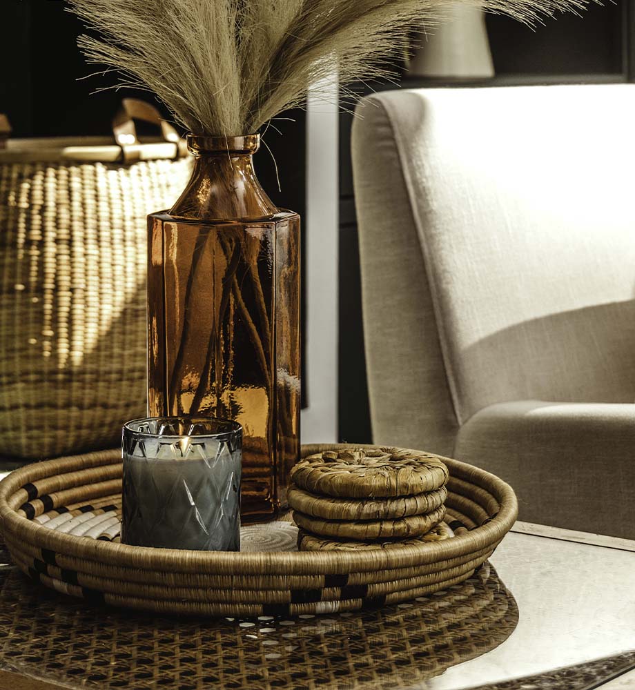 Black, White and tan tray with candle, banana leaf coasters, and orange vase inside. 