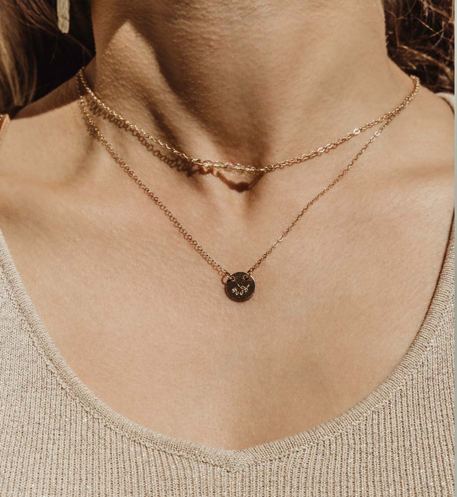 Two gold necklaces around women's neck wearing a beige top