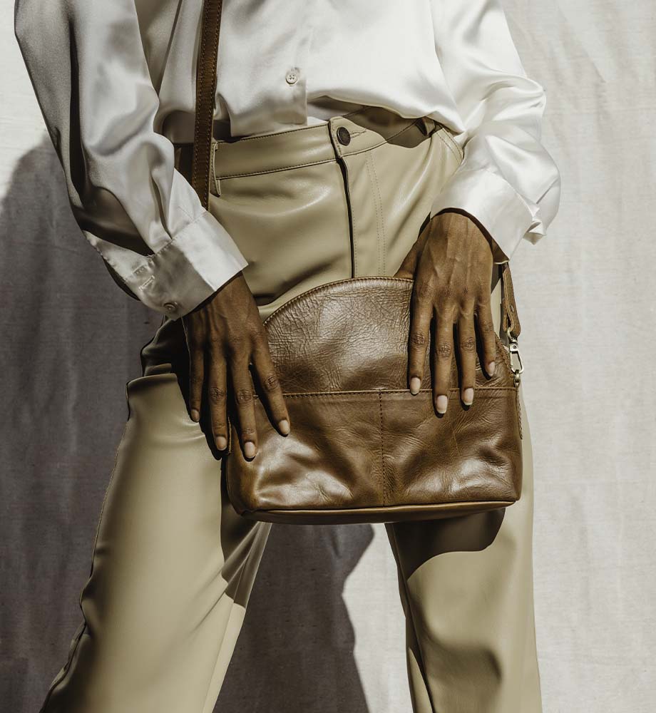 Women wearing white silk top with beige leather pants holding a leather halfmoon bag