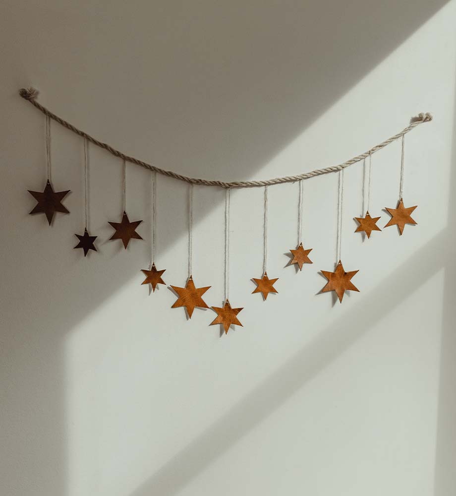 Leather and string star garland hanging on white wall with shadows.