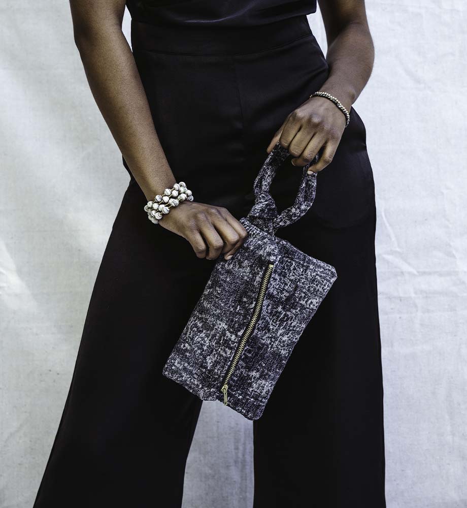 Women wearing a black jumpsuit while holding a nacy blue clutch and a neutral wrap bracelet