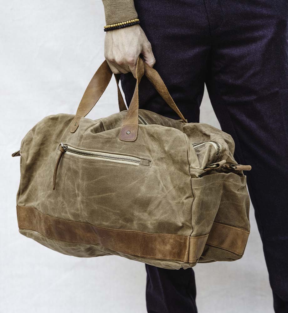 Tan canvas duffle bag with zipper being carried by a man with dark plans on 