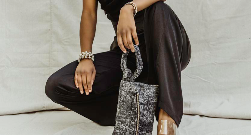 Woman crouching down with navy clutch and black jumpsuit.