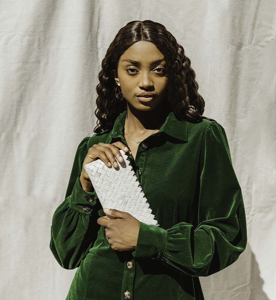 women with wavy hair holding a white upcycled clutch while wearing a green dress