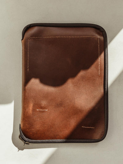 Dark brown leather exterior of the Expedition Travel Tech Case with black zipper on white surface. 