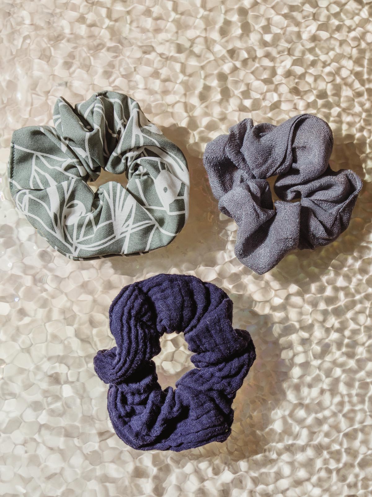 Three scrunchies laying on a table - one is blue, one is darker blue, one is green