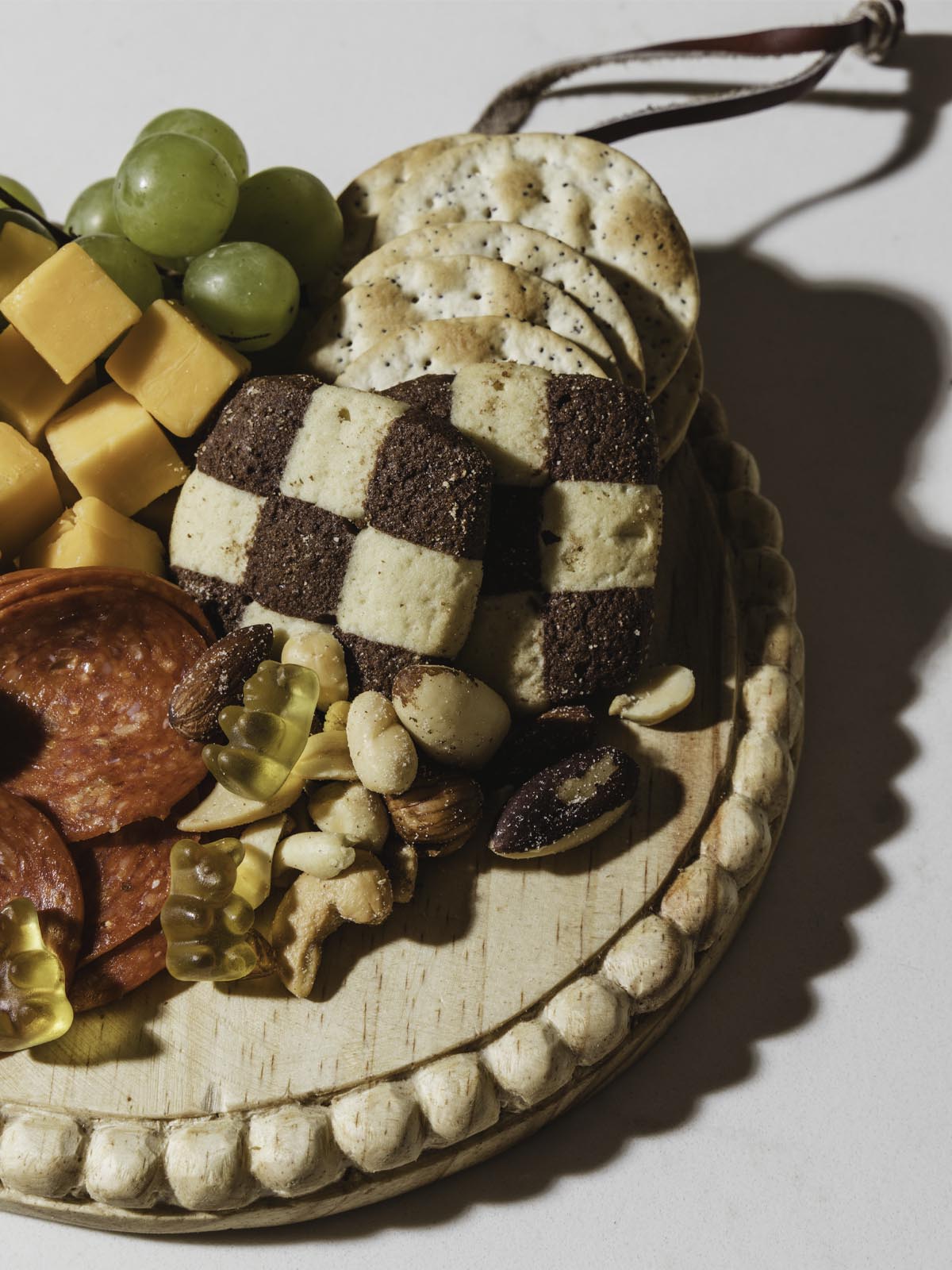 Round wooden board with cookies, crackers, cheese, meat and grapes on top of it