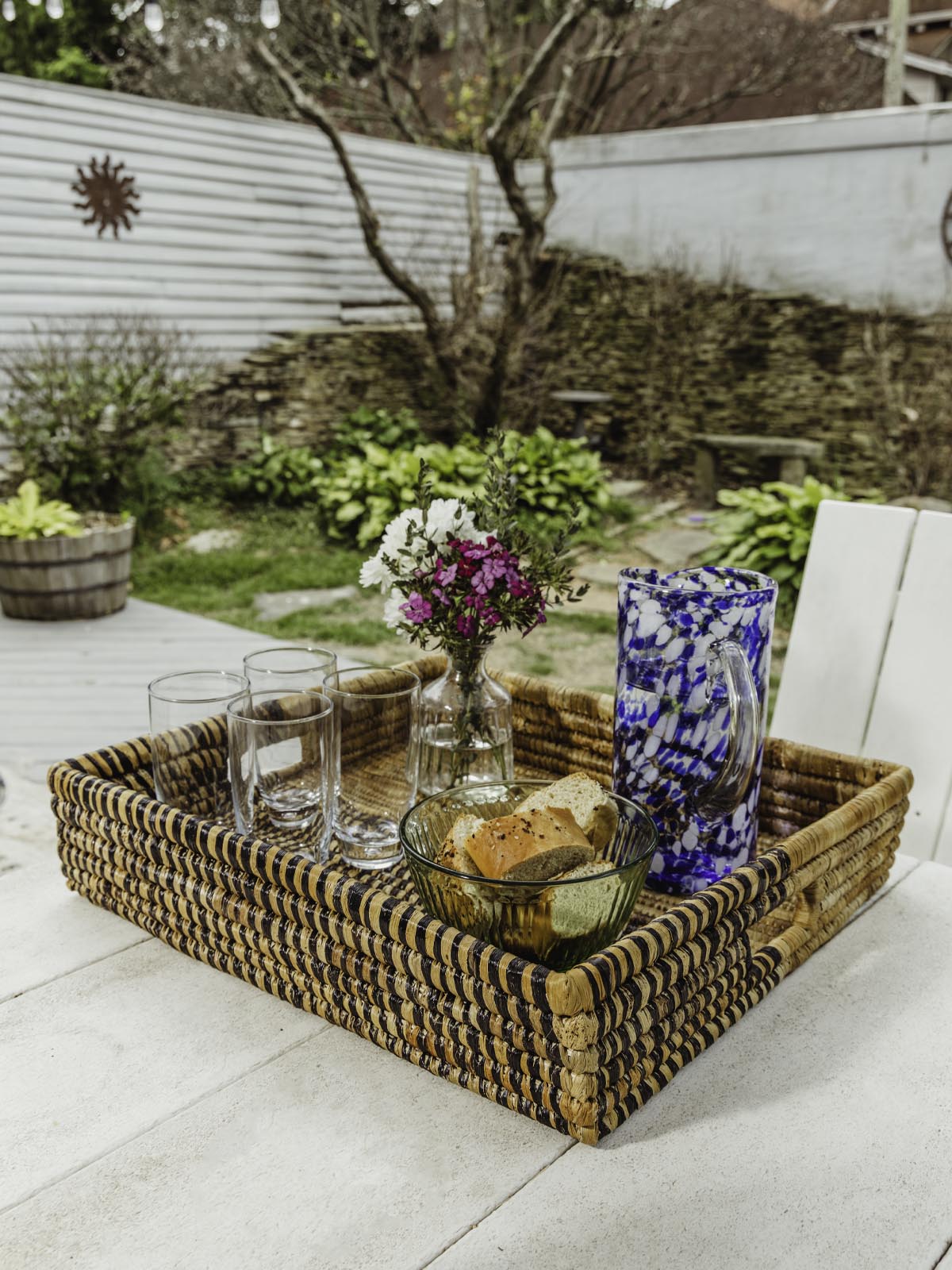 Square woven basket on white table with glasses, flowers and bread inside. 