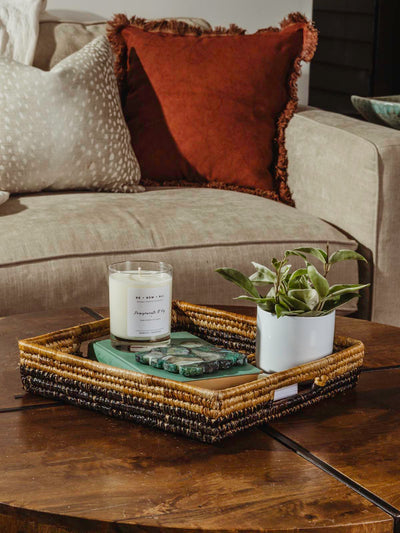 Square woven basket on a coffee table with plant and candle inside. 