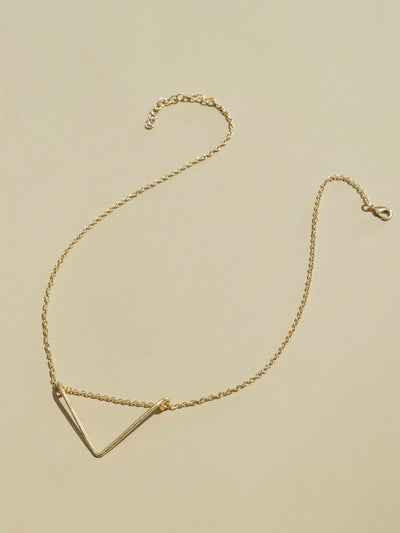 Crowned  free gold necklace with triangular shaped pendent on tan background.