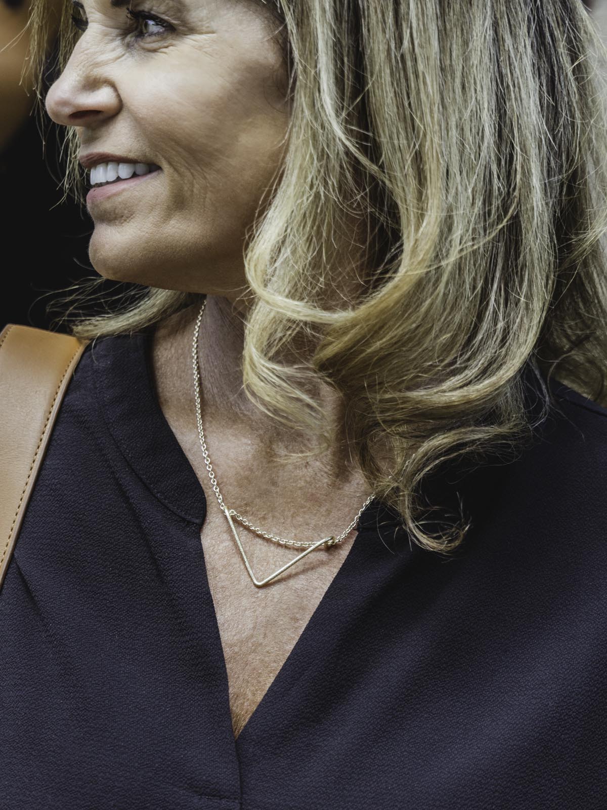 Tightly cropped image of a female model in black top wearing Crowned  free gold necklace with triangular shaped pendent.