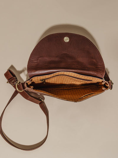 Image of interior detail of Joyn crossbody brown leather purse. Interior is made of pattern cloth and features pockets and a zipper pocket.