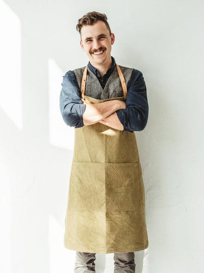 A man wearing a tan apron in from of a white wall