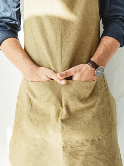 A man wearing a tan apron in from of a white wall
