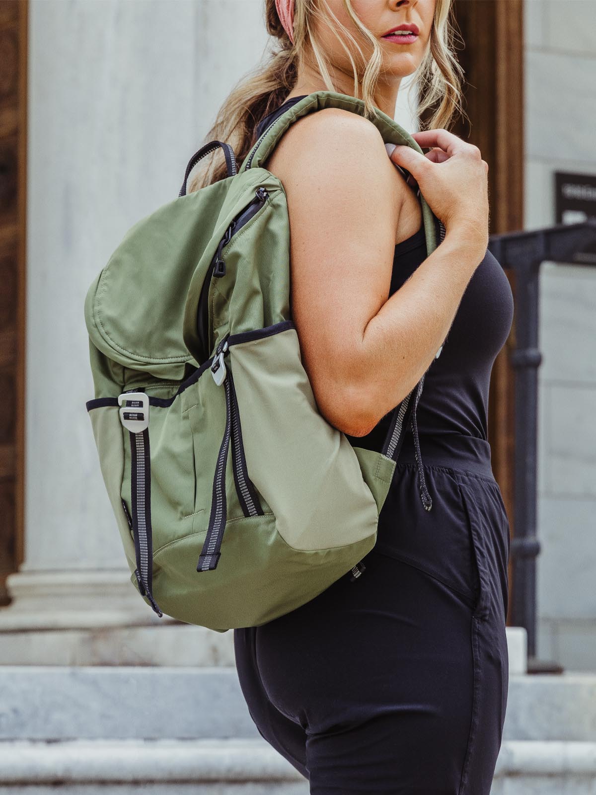 Woman standing outside, wearing green Aruna Project backpack.