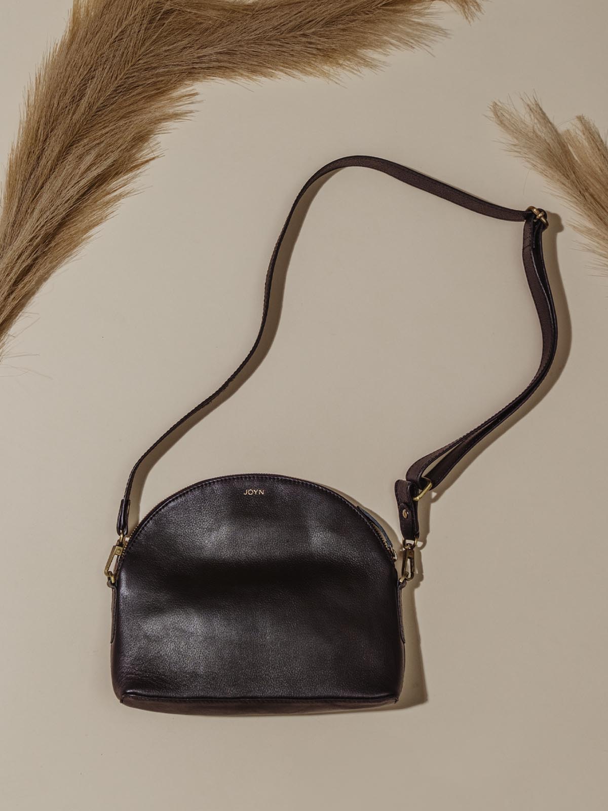 Black leather semi circle handbag laying on tan background. 