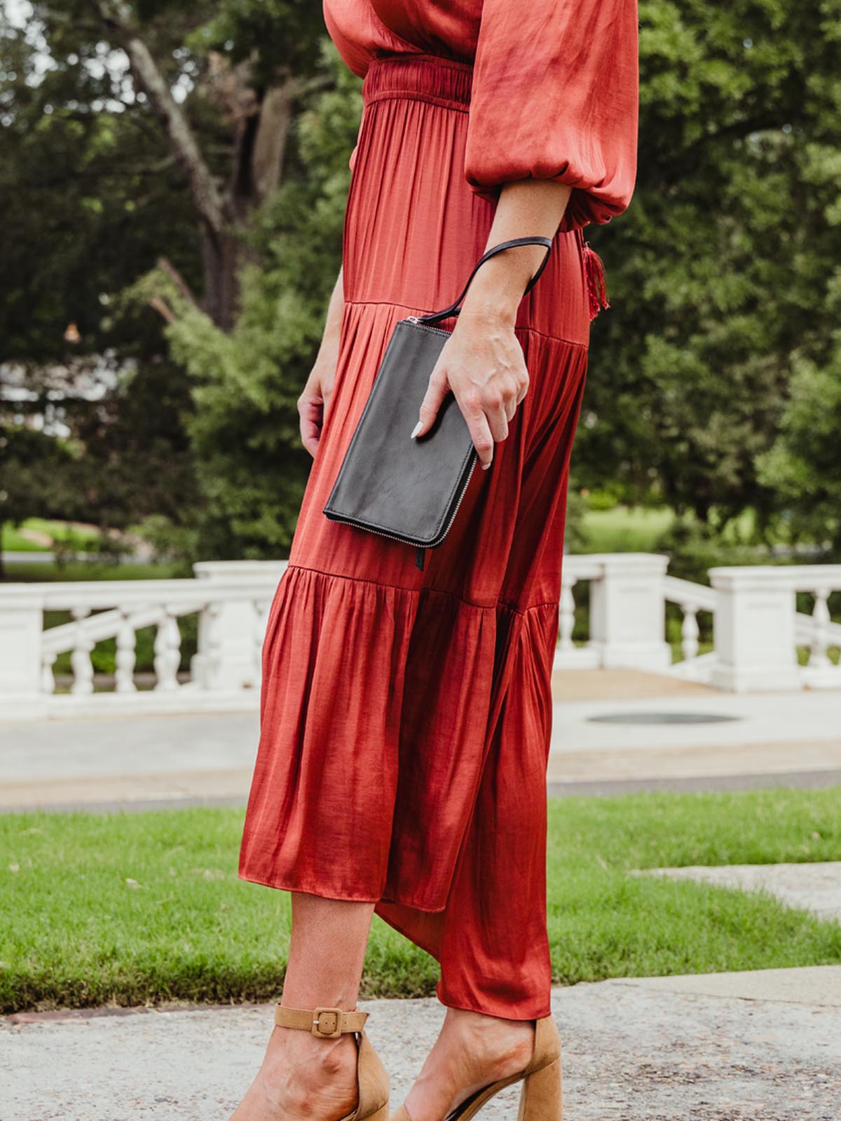model wearing red dress while holding black clutch wallet