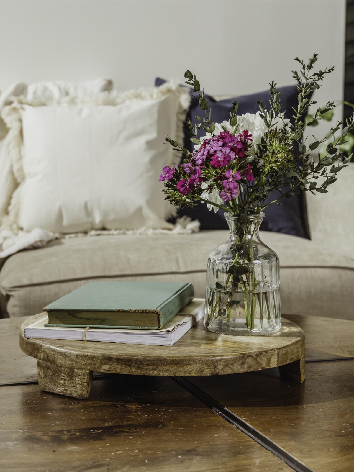 Large wood tray with books and flower vase atop while placed on a coffee table. 
