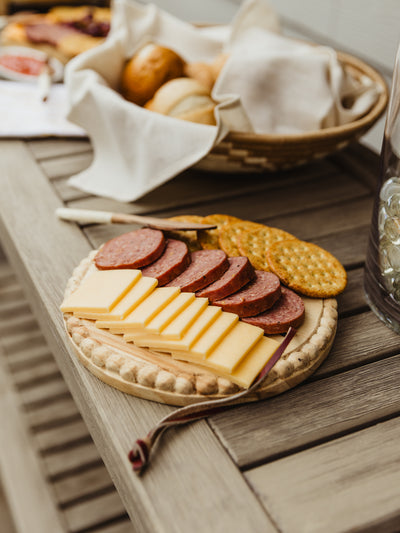 Round wood charcuterie board with food it place on an outdoor table. 