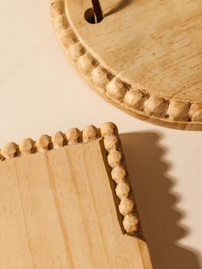 Detail of hand carving on round and rectangular wooden charcuterie board on cream background.