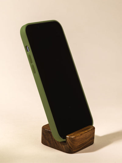 Wooden cell phone stand holding phone vertically on cream background.