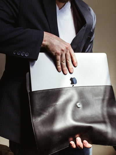 Male model with face not visible putting laptop in black leather laptop sleeve. 