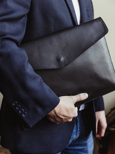 Male model holding black leather laptop sleeve with envelope style opening and metal snap. 