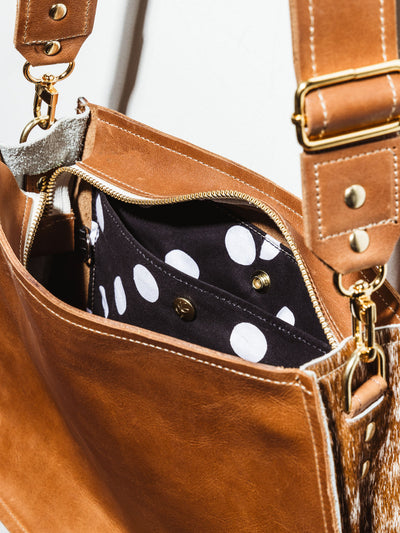 Interior of the Brown Leather Messenger Bag. The interior consists of a snapping pocket and black and white polkadot fabric. 