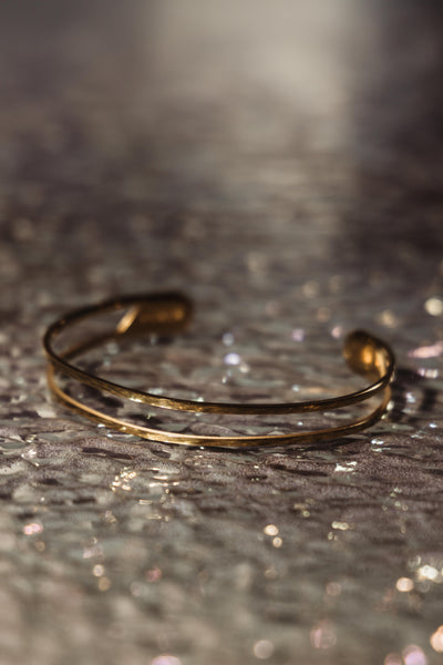 Close shot of gold cuff bracelet on reflective surface.