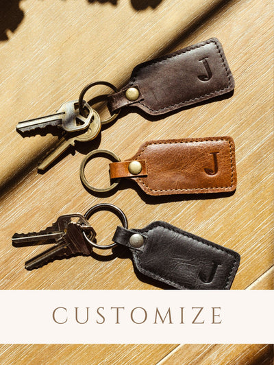 Leather Keychains with keys on wood table. Digital sticker indicates products are customizable.