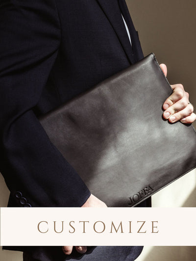 Male model in suite without face visible holding leather laptop case showing customizable label. Digital sticker to indicate the product is customizable. 