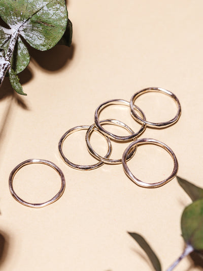 Set of 6 sterling silver stacking rings on cream background with dried leaves for styling.