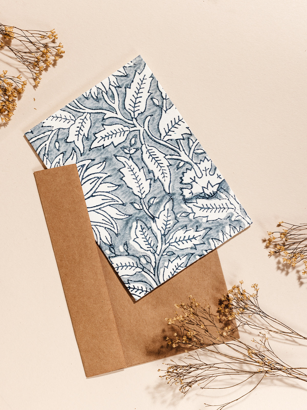 Hand drawn blue floral stationary with parchment brown envelopes on cream surface with dried flowers.