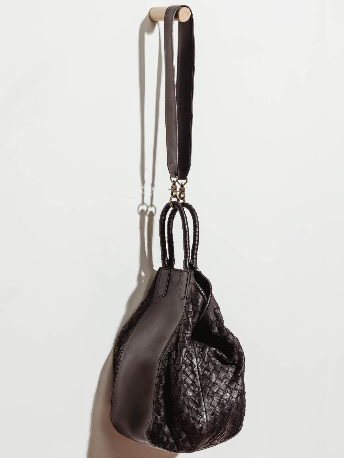 Black leather all day clasped shut, hanging by shoulder strap on white wall