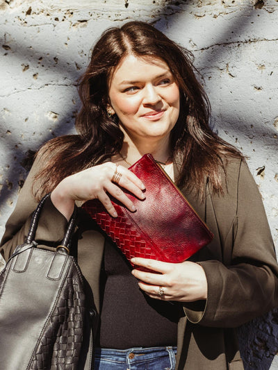 Female model holding red leather pouchette with black leather handbag. 