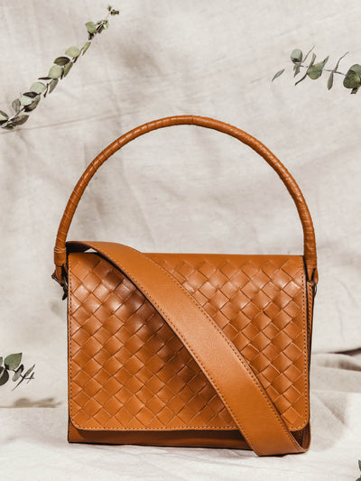 Handmade braided leather bag on cloth background with some minimal greenery.