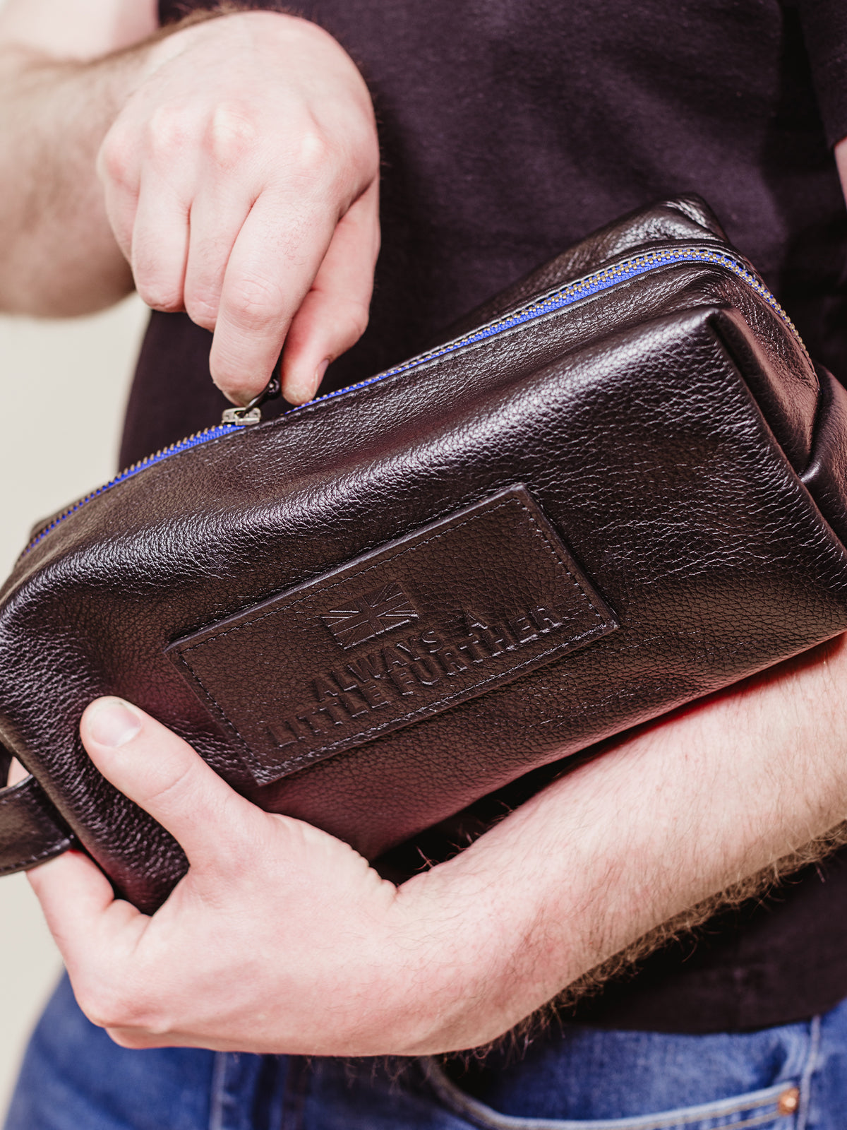 Male model unzipping black leather toiletry bag with blue accent zipper. 