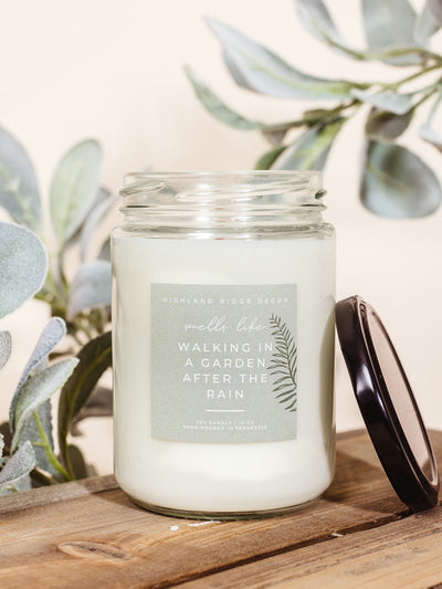 Walking in the Garden scented candle on a wooden surface with greenery for styling. 