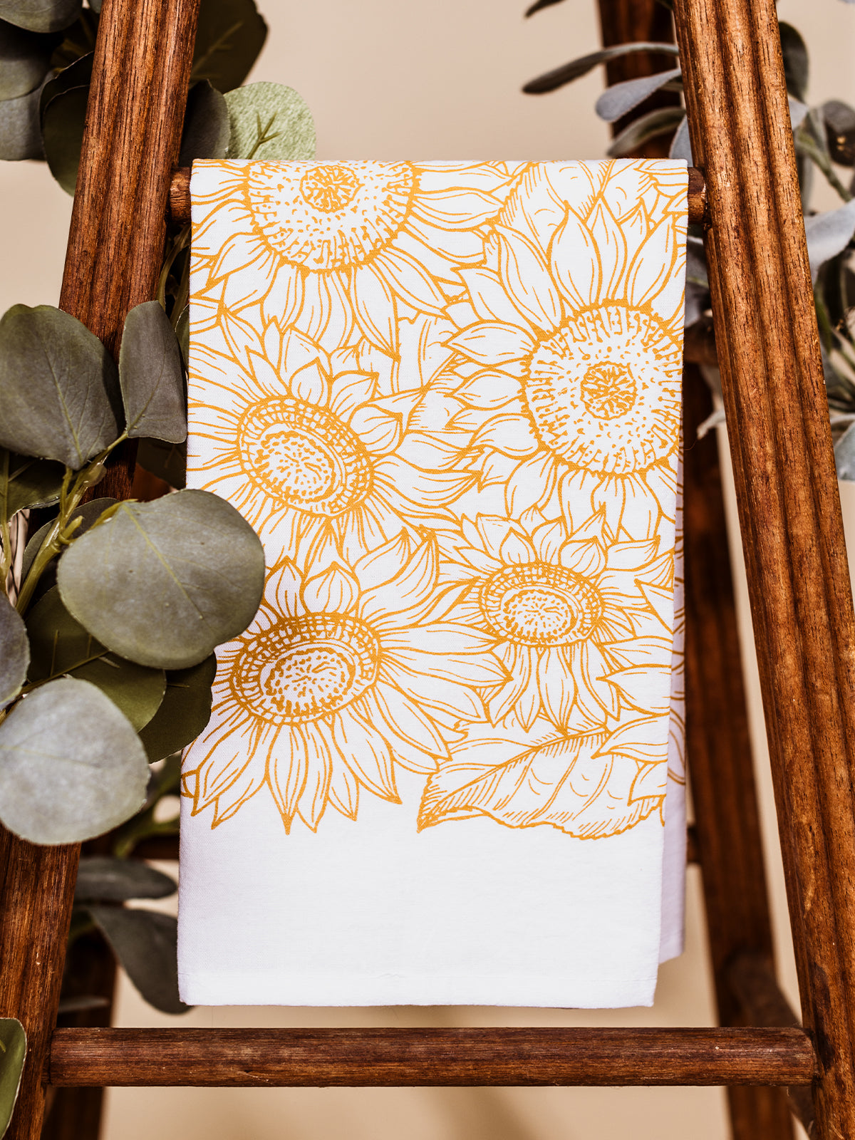 Sunflower tea towel dropped on a wooden stool with greenery.