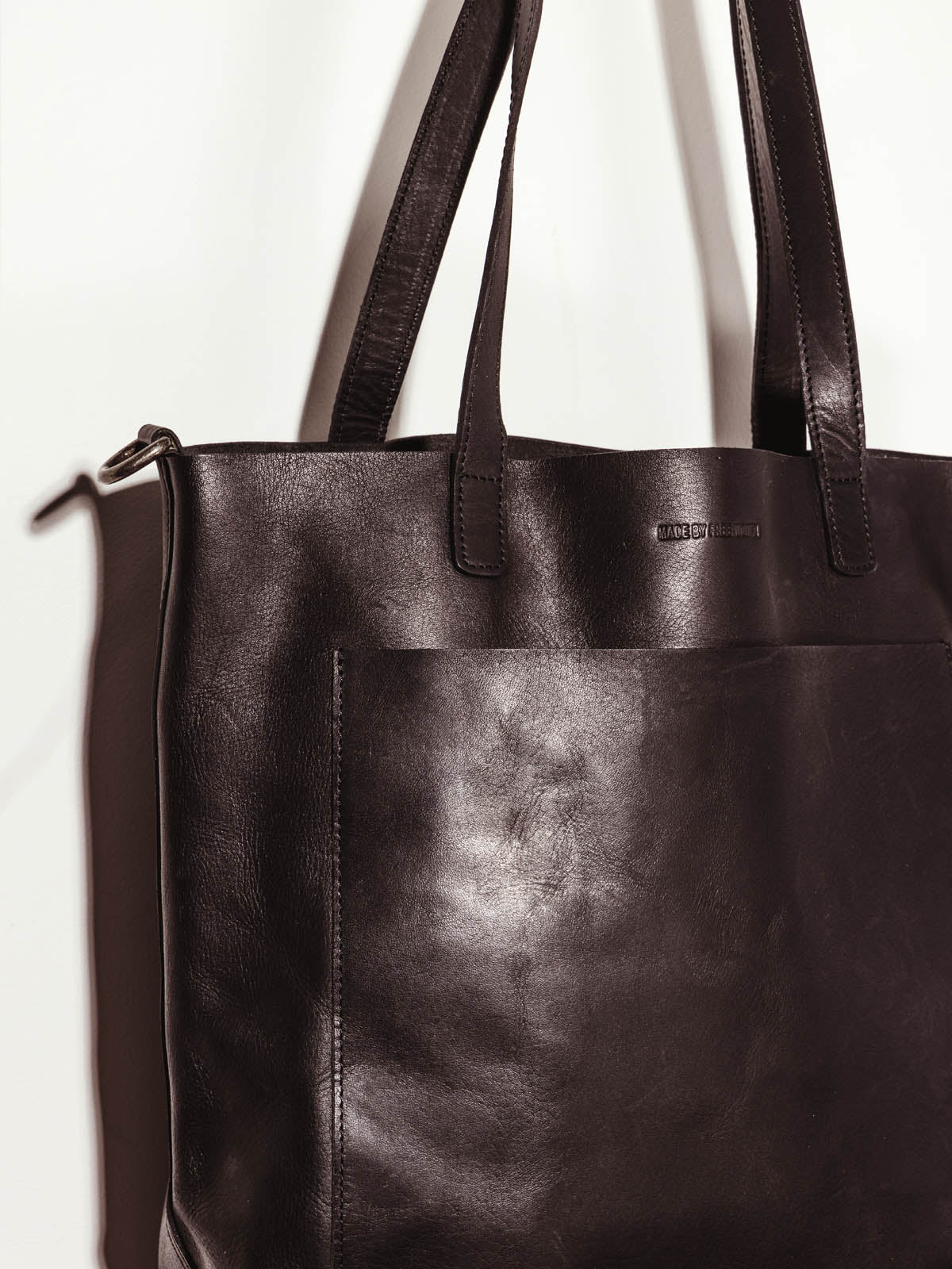 Made Free large black leather hand bag on white background showcasing hand  straps and leather working details.