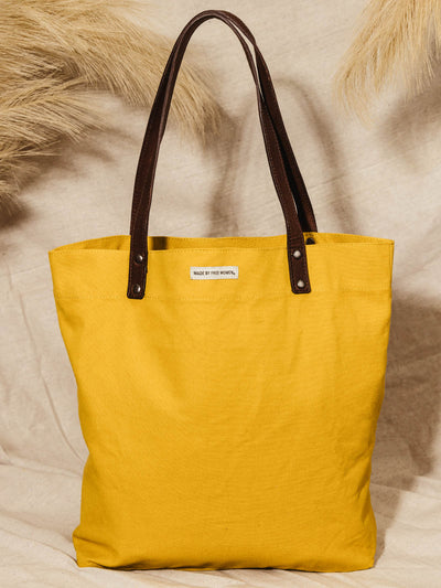 Made free yellow tote bag with leather straps on canvas cloth bag ground with dry plants.