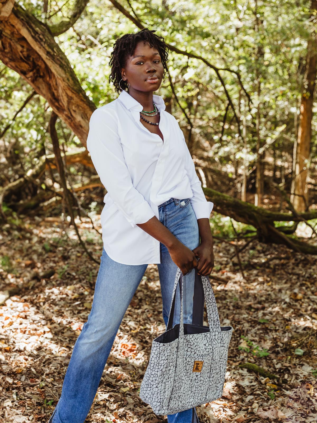 Tall African American female model in a nature background with grey New Hope Girls tote bag. 