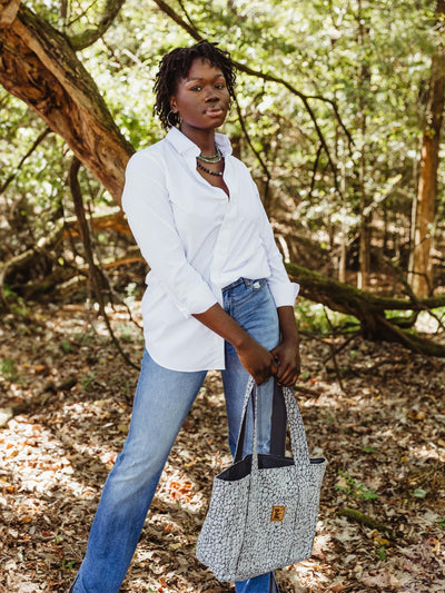 Tall African American female model in a nature background with grey New Hope Girls tote bag. 