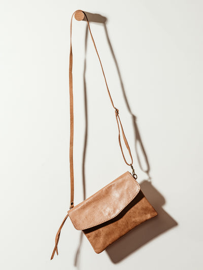 Brown leather Crossbody Clutch on white wall.