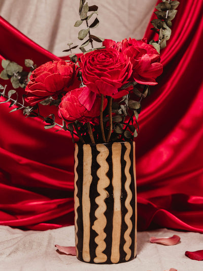 Black and white hand made vase with red roses on cloth table with red silk drapery. 